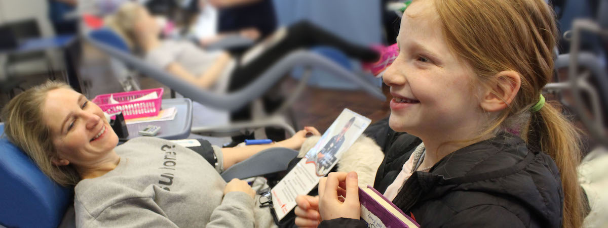 Photo of mother donating blood with her daughter by her side